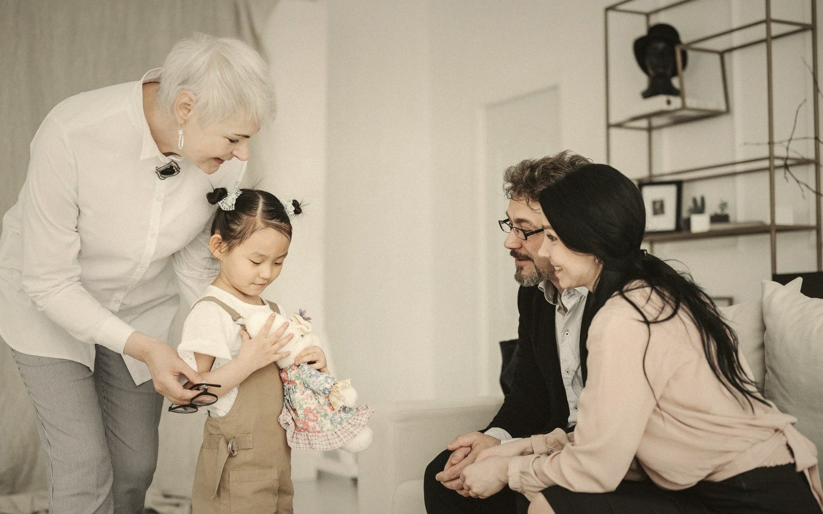 A young girl holds a stuffed toy while family members watch and smile in a living room