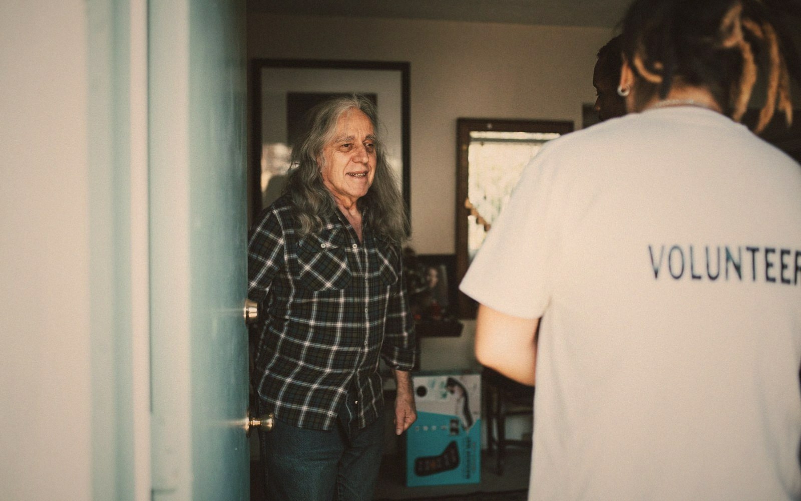 An older woman greets a volunteer wearing a "volunteer" t-shirt at her front door
